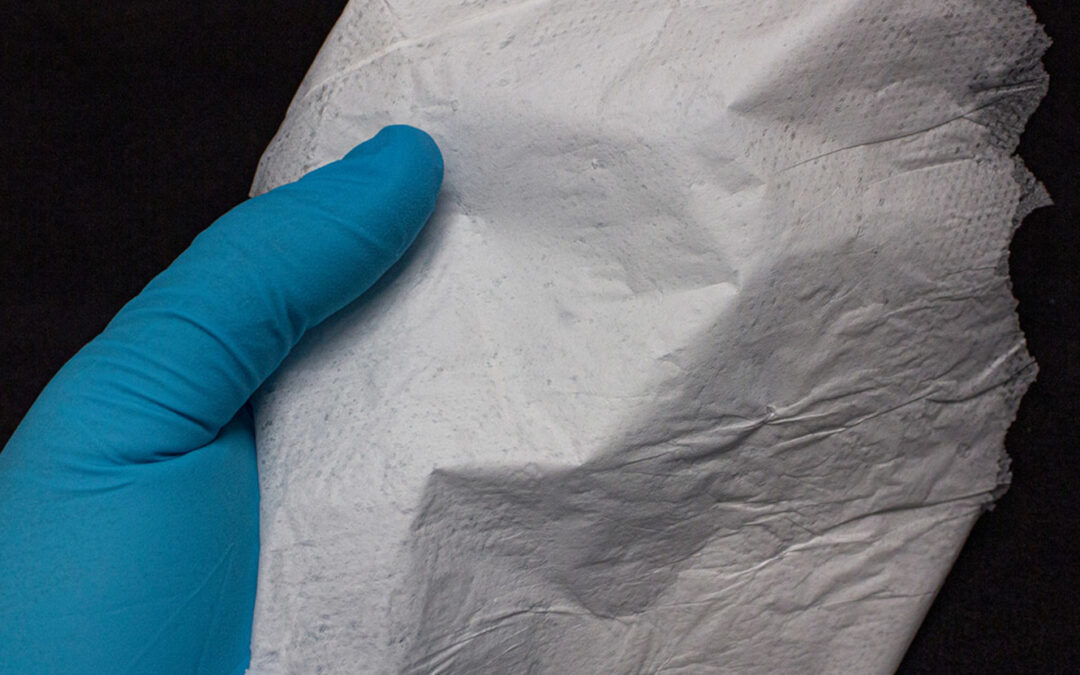 Eine behandshuhte Hand hält ein weißes Gewebe, das einem Papiertaschentuch ähnelt.