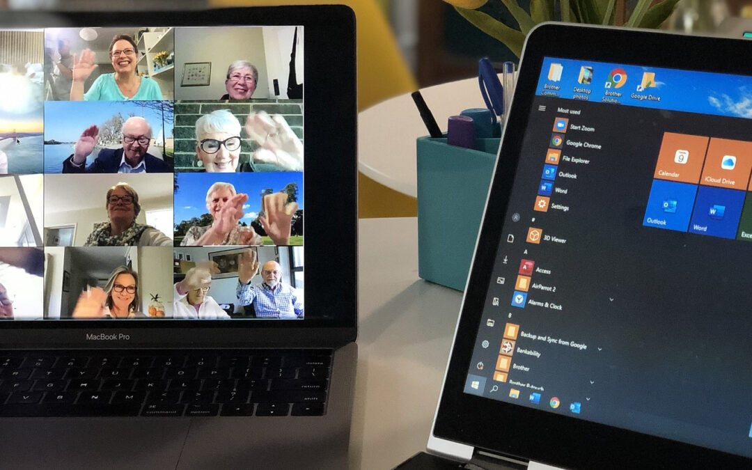 2 aufgeklappte Laptops nebeneinander auf dem Tisch. Der linke zeigt viele winkende Gesichter in einem Online-Meeting.