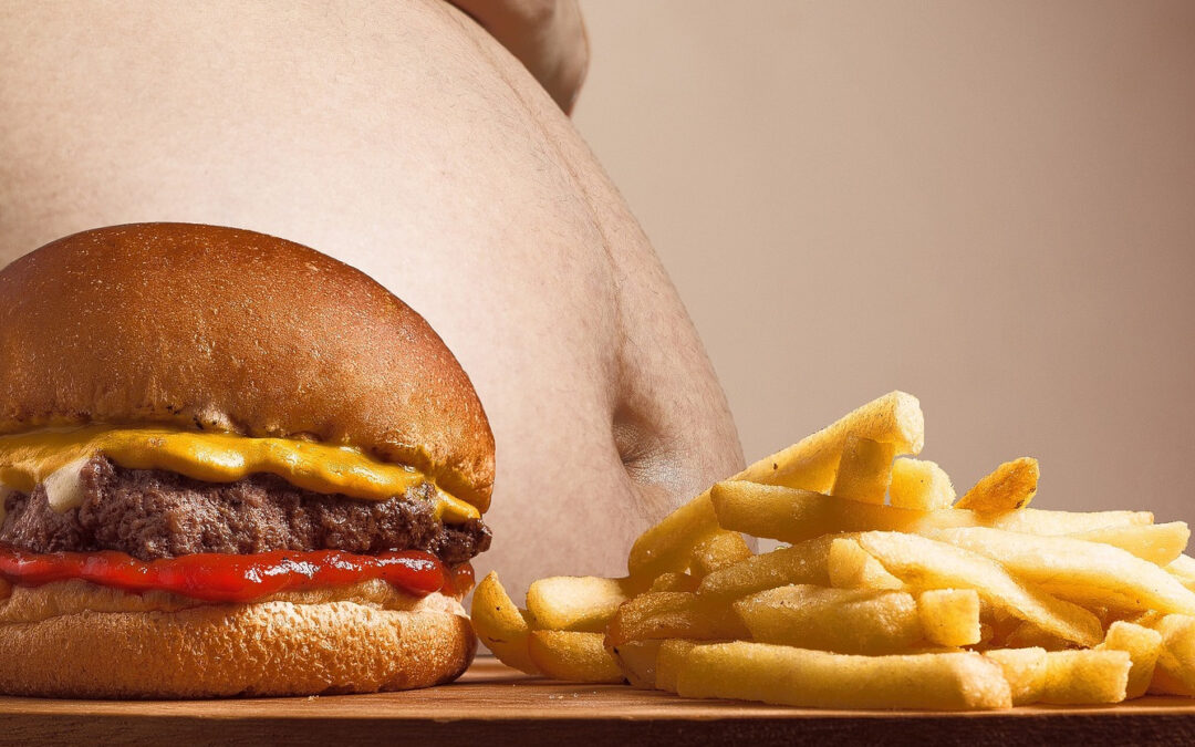 Ein Fast-Food-Teller mit Burger und Pommes. Im Hintergrund ein nackter, dicker Bauch