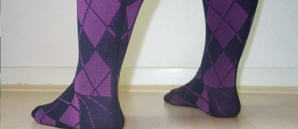 Flachgestrickte Kompressionsstrümpfe zur Kompressionstherapie mit Naht und Rautenmuster in violett. Im Bild zu sehen: Etwas dickere Frauenbeine von Fuß bis Wade, bekleidet mit den beschriebenen Strümpfen.