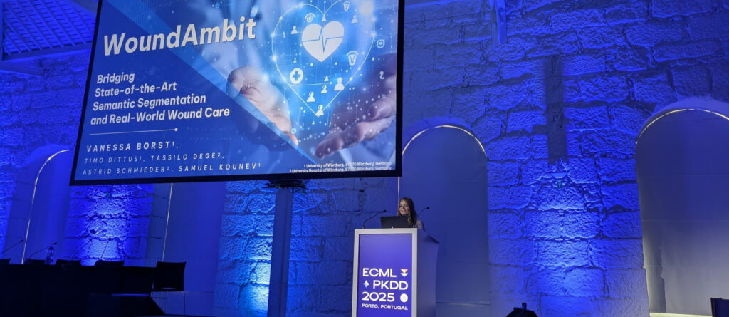 Für ihr Projekt WoundAmbit wurde die Informatikerin Vanessa aus Würzburg auf der der ECML PKDD mit dem “Best Student Paper Applied Data Sciences Track” ausgezeichnet. Blick auf die in blauem Licht erstrahlte Bühne mit Rednerpult und großer Leinwand.