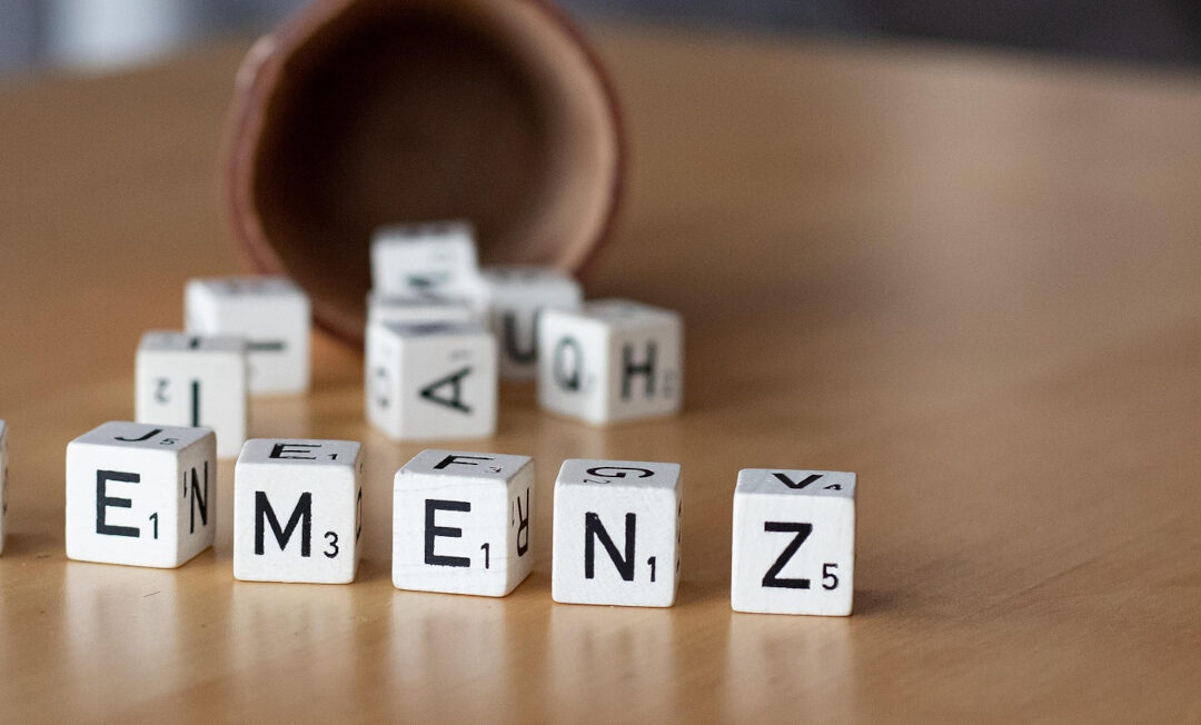 Scrabble-Steine, die aus einem im Hintergrund liegenden Würfelbecher gefallen sind, formulieren das Wort "Demenz".