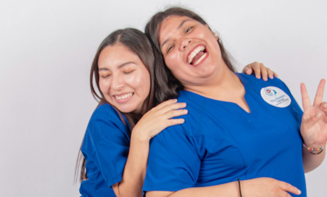 2 Pflegekräfte, die sich lachend in den Armen liegen.