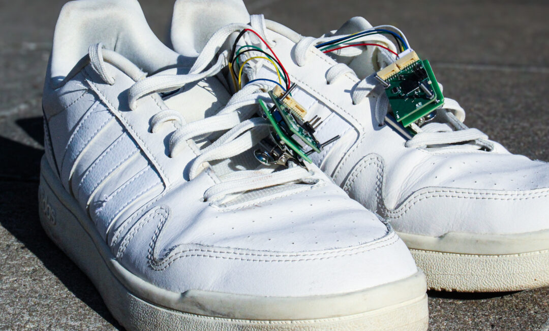 Ein paar Sportschuhe. Am Schnürsenkel hängt eine Platine. auch dünne Kabel sind sichtbar.