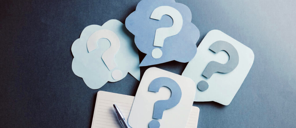 Sprechblasen aus Papierblättern, auf denen Fragezeichen aus Papier liegen.