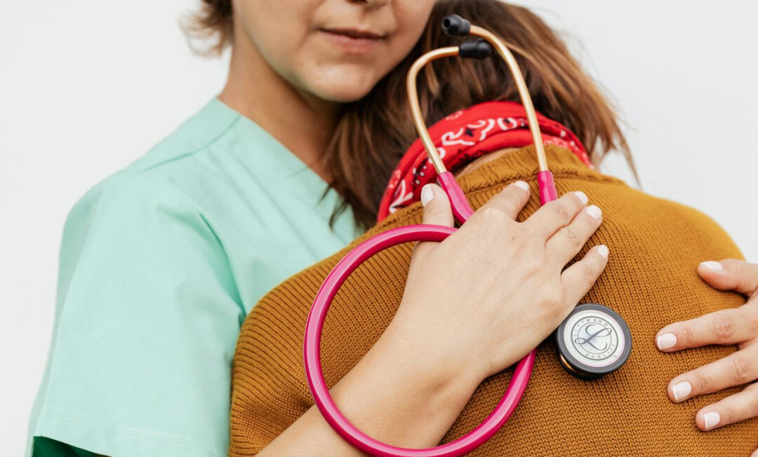 Eine Ärztin oder Pflegekraft mit Stethoskop in der Hand nimmt eine ältere Patientin tröstend in den Arm.