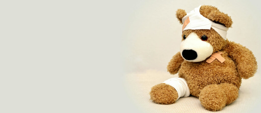 Ein Teddy mit Verbänden am rechten Bein und am Kopf sowie einem Pflaster auf der Schulter.