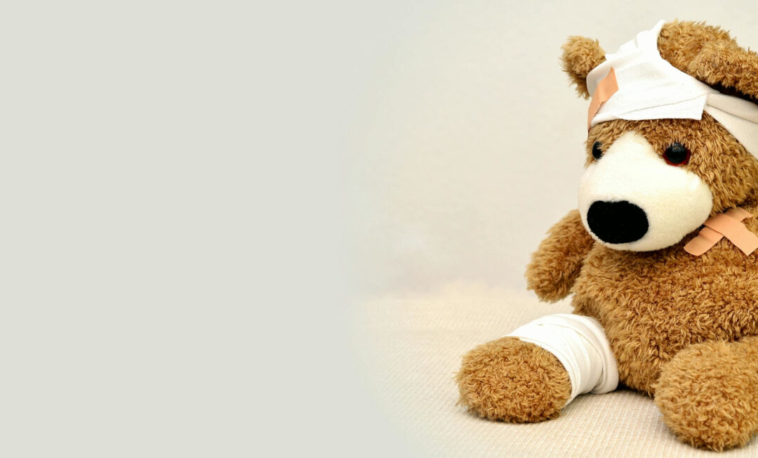 Ein Teddy mit Verbänden am rechten Bein und am Kopf sowie einem Pflaster auf der Schulter.